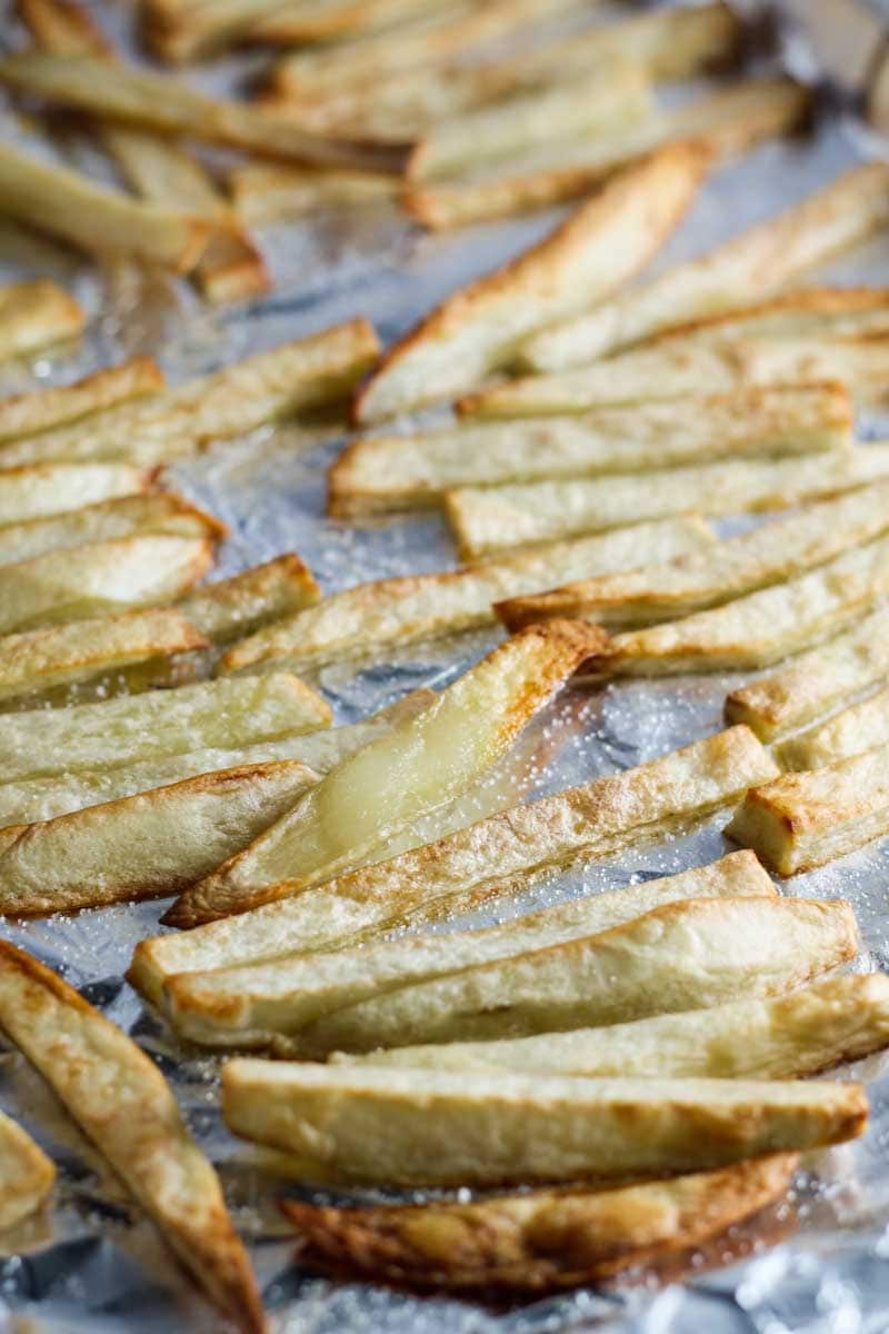 Homemade fries sprinkled with salt on a foil-covered sheet pan.