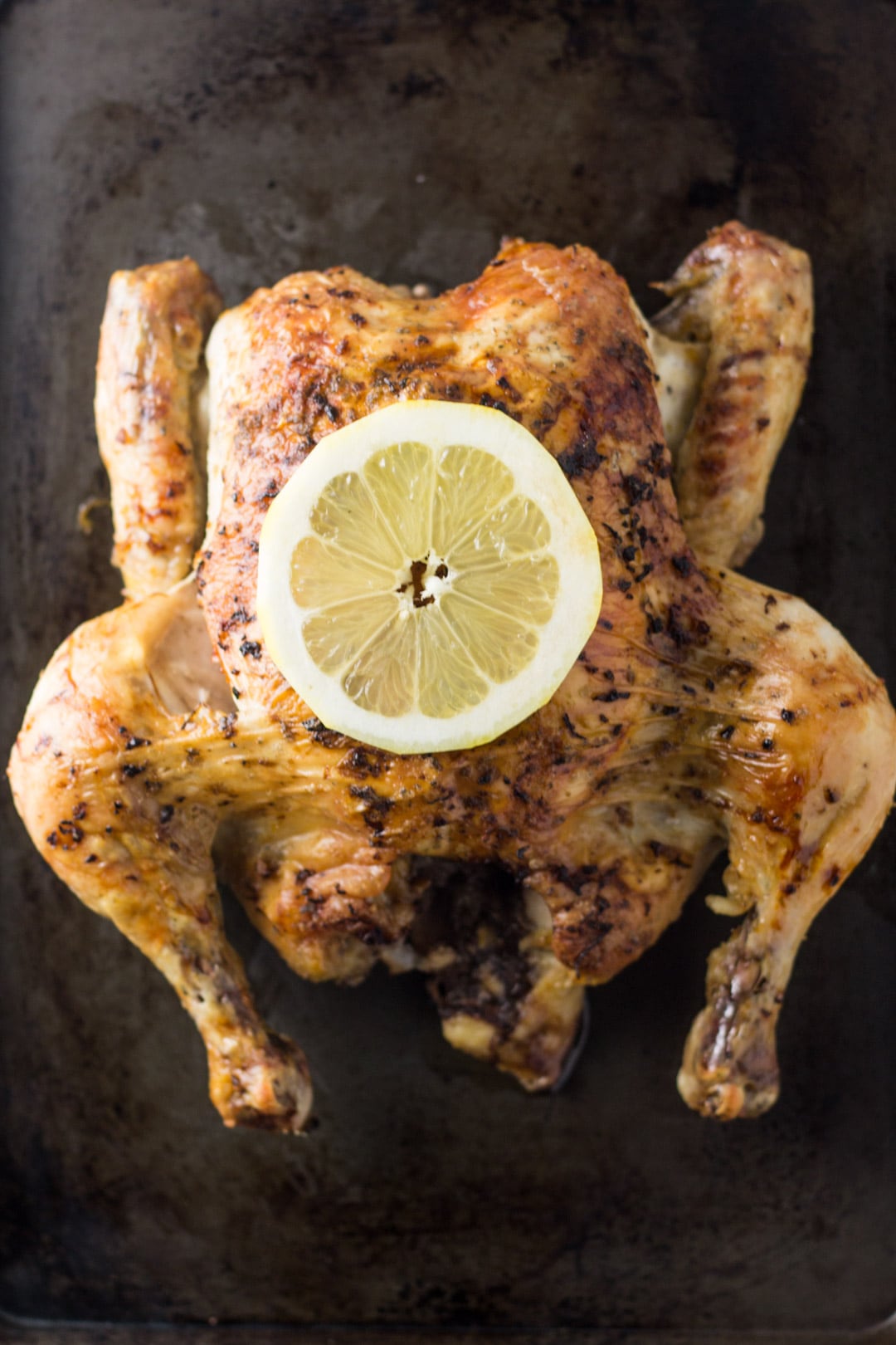 Looking down at a lemon roasted whole chicken topped with a lemon slice.