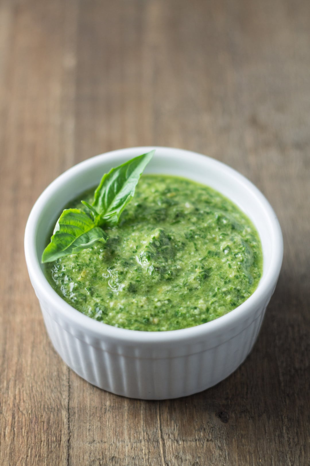A small bowl filled with homemade pesto and garnished with a couple of basil leaves.
