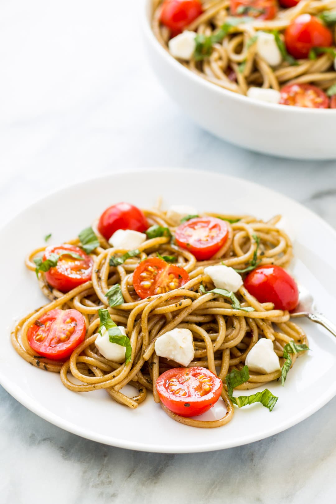 A plate of caprese pasta salad made with gluten-free spaghetti, mozzarella, cherry tomatoes, balsamic vinegar, and basil.