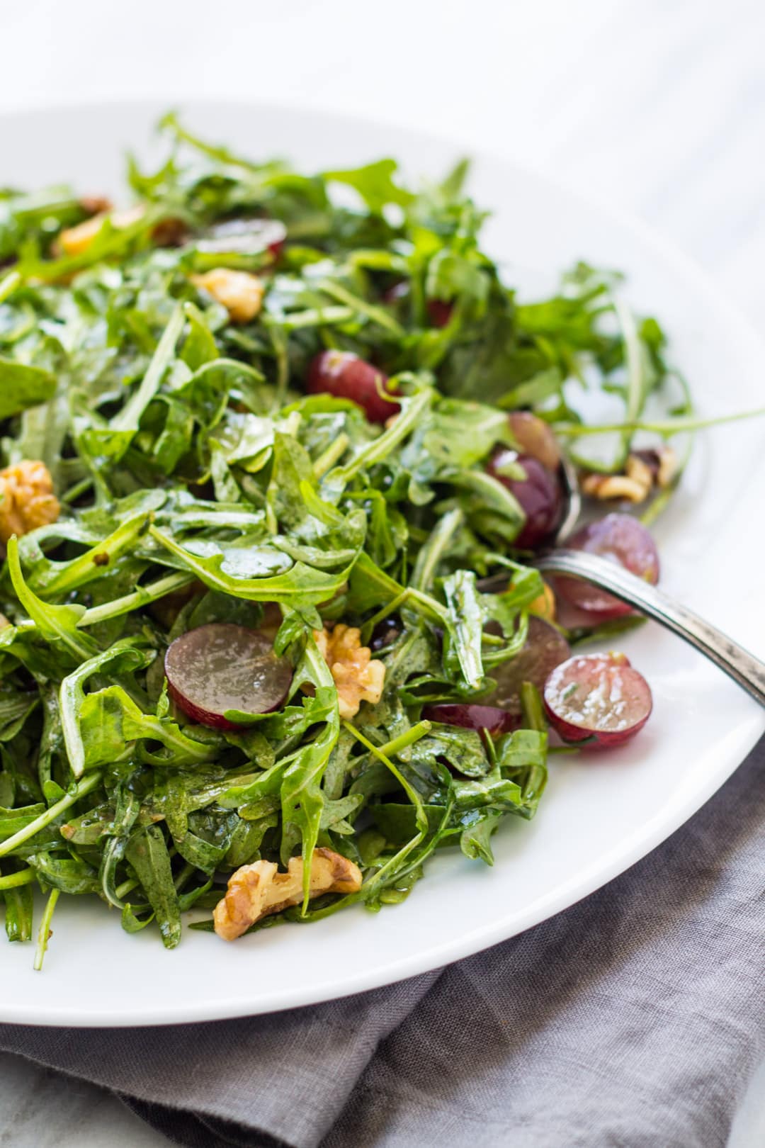 A lightly-dressed salad with arugula, halved grapes, and walnuts.