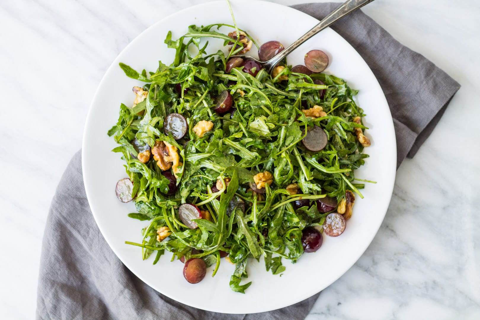 Looking down at a plate of arugula salad with grapes and walnuts.