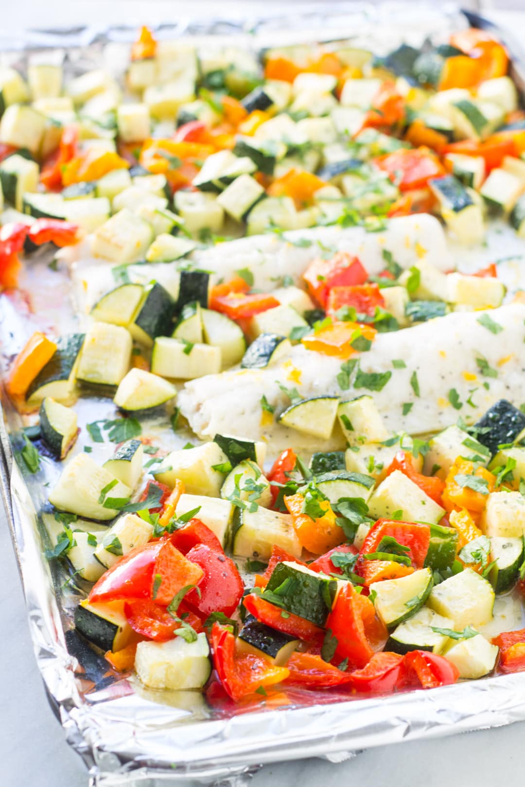 A sheet pan with baked cod, zucchini and bell peppers flavored with lemon and parsley.