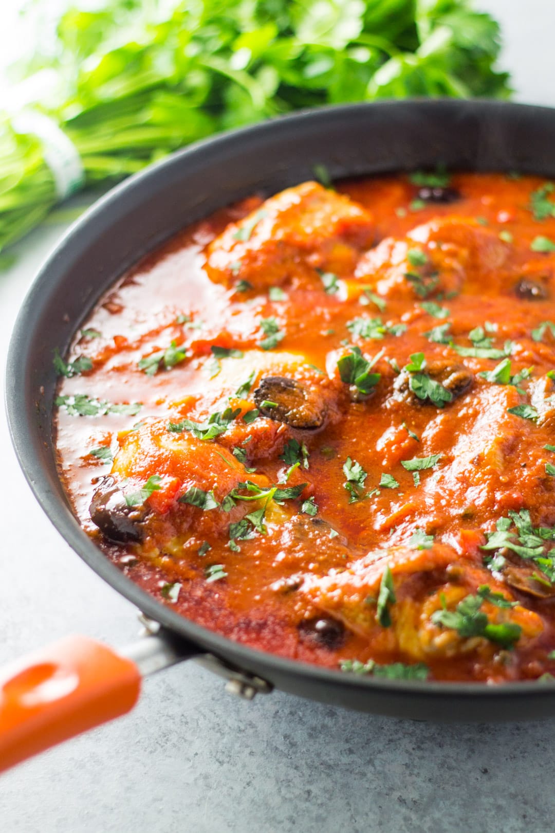 A skillet filled with chicken cooked in a tomato sauce and topped with fresh parsley.