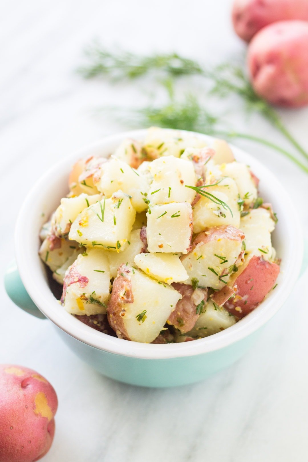 Light blue bowl filled with a cold potato salad flavored with lemon and dill.