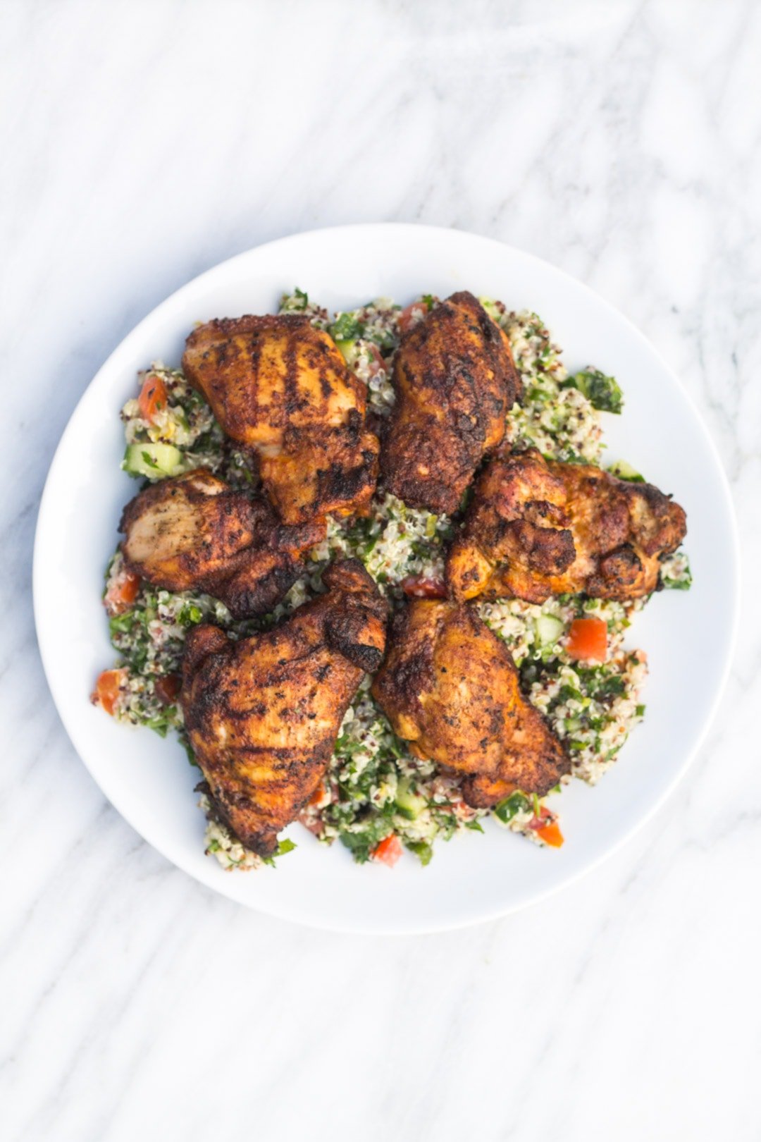 Looking down at a plate filled with quinoa tabbouleh and topped with grilled marinated chicken 