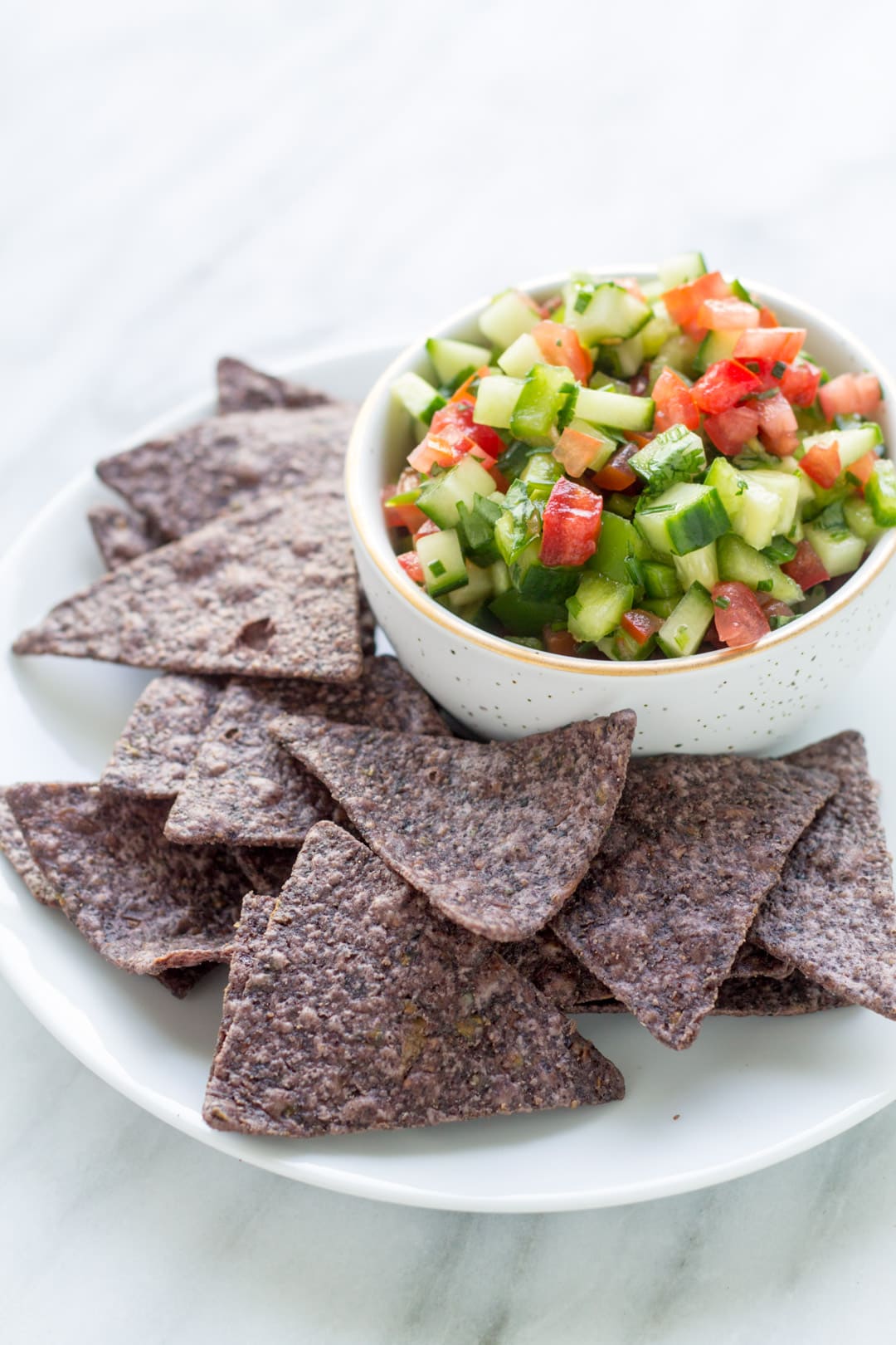 A close up of fresh low FODMAP salsa in a small bowl surrounded by blue corn chips.