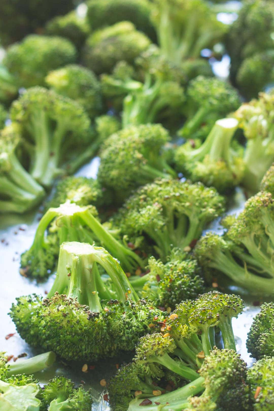 Roasted broccoli sprinkled with red pepper flakes on a sheet pan lined with aluminum foil.