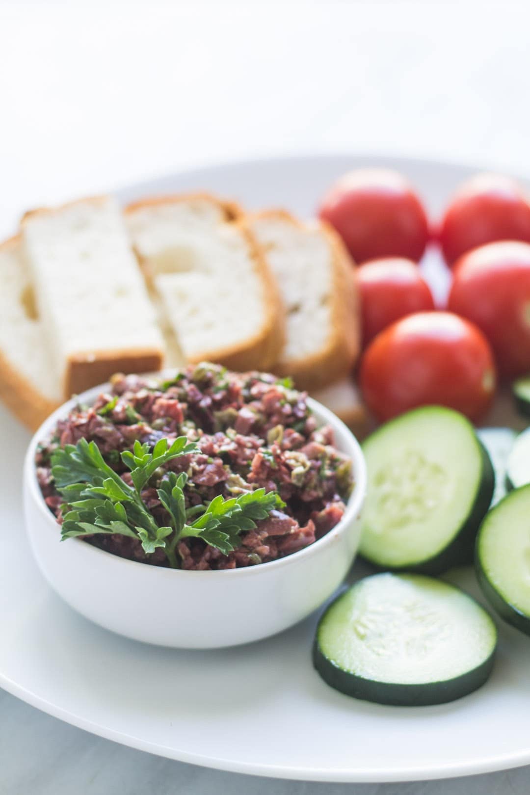 Bowl of low FODMAP olive tapenade surrounded by veggies and gluten-free bread