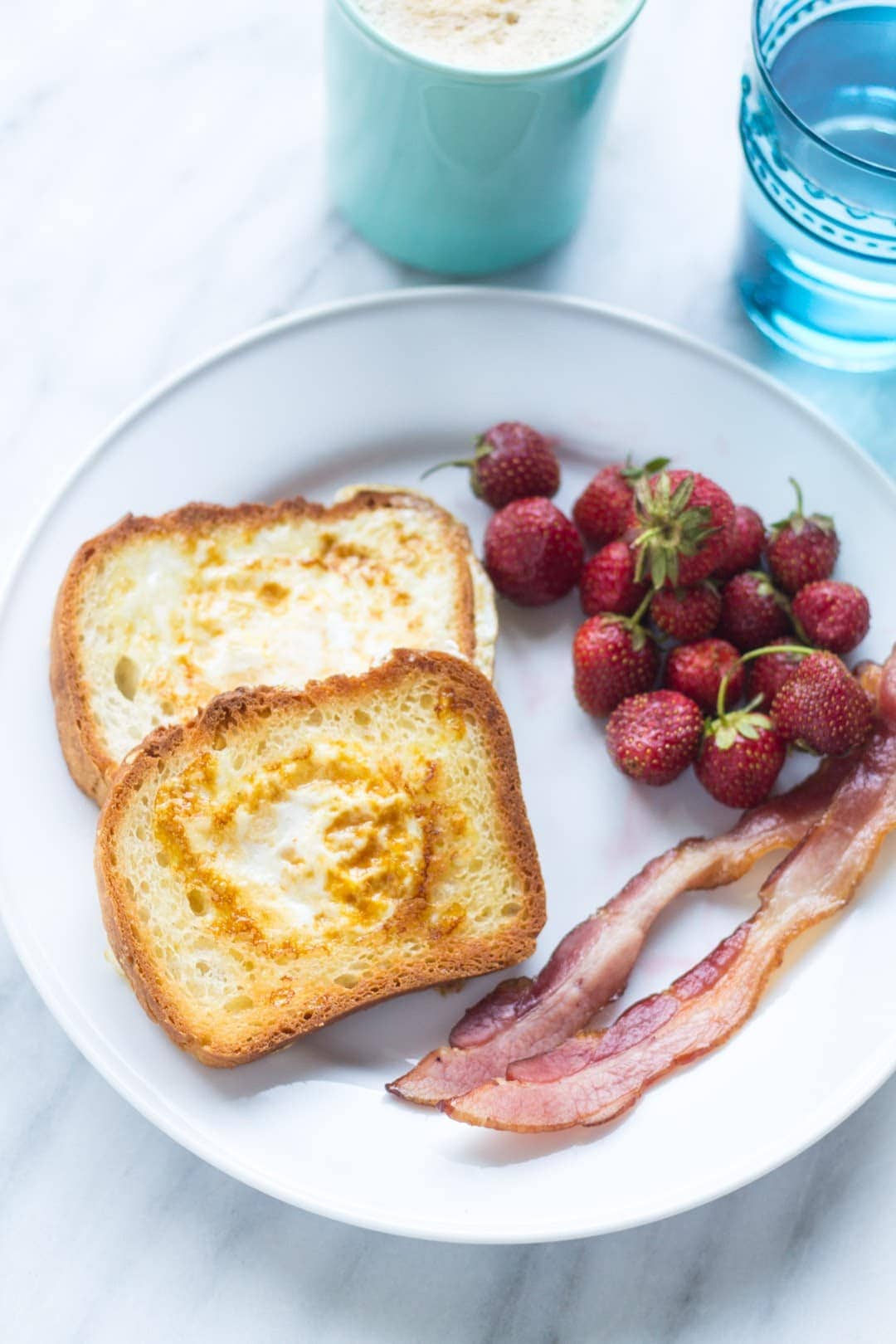 Plate of low FODMAP toad in a hole (toast with a cooked egg in the center), slices of bacon and strawberries