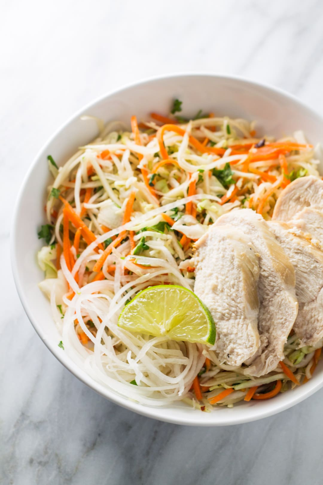 Bowl of low FODMAP Thai citrus salad topped with chicken and a lime wedge