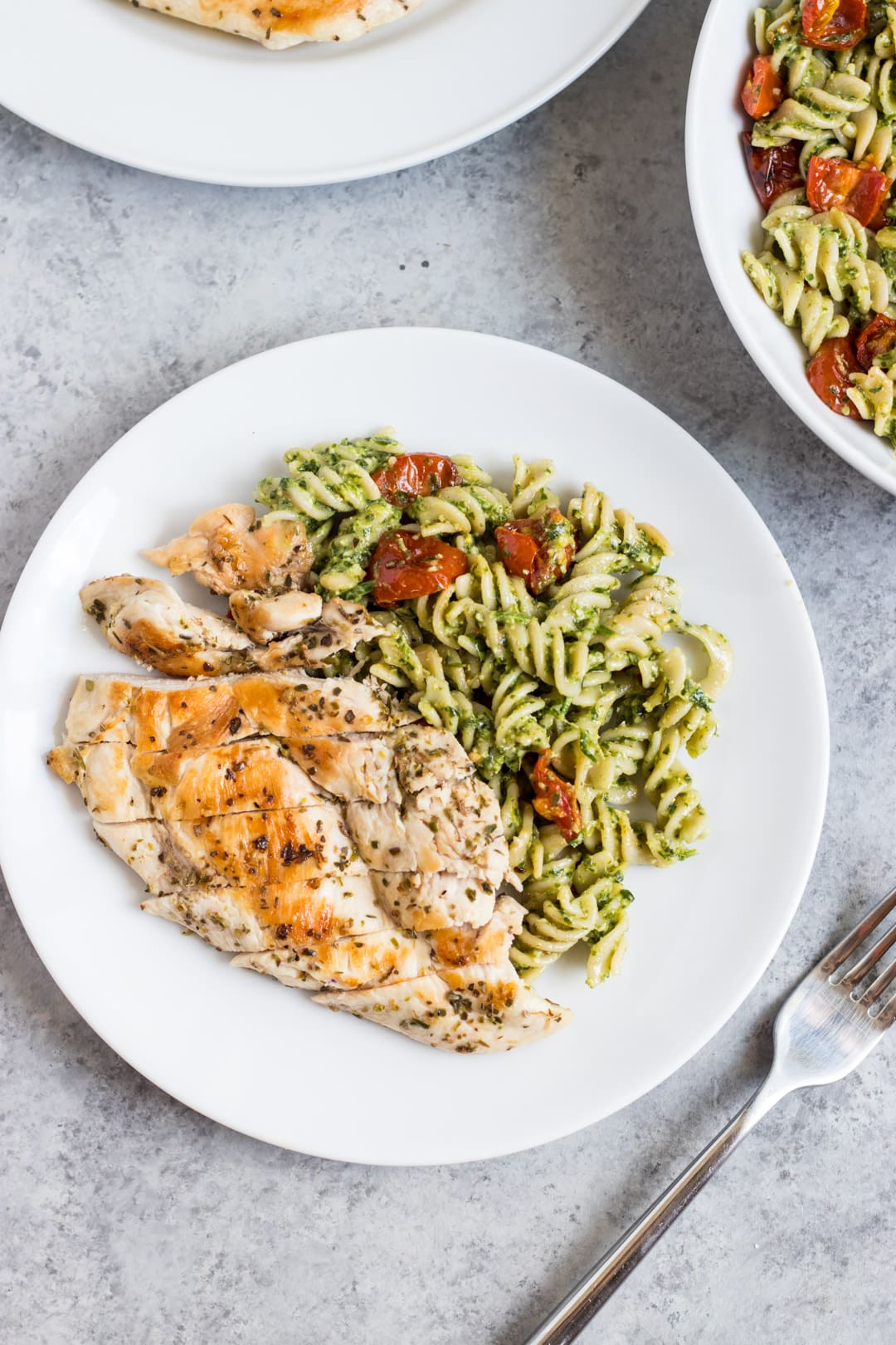 Looking down at a plate of Low FODMAP Pesto Pasta with Grilled Chicken and Roasted Tomatoes