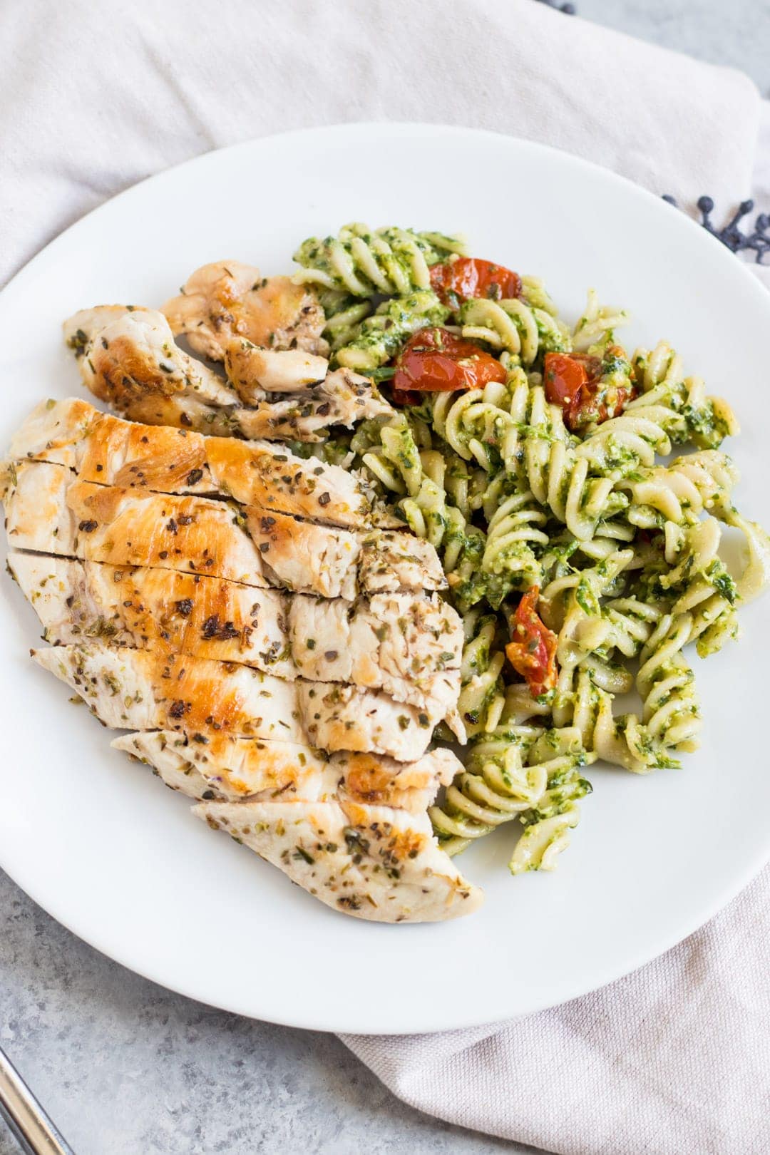 A plate of pesto-tossed pasta, grilled chicken and roasted tomatoes.