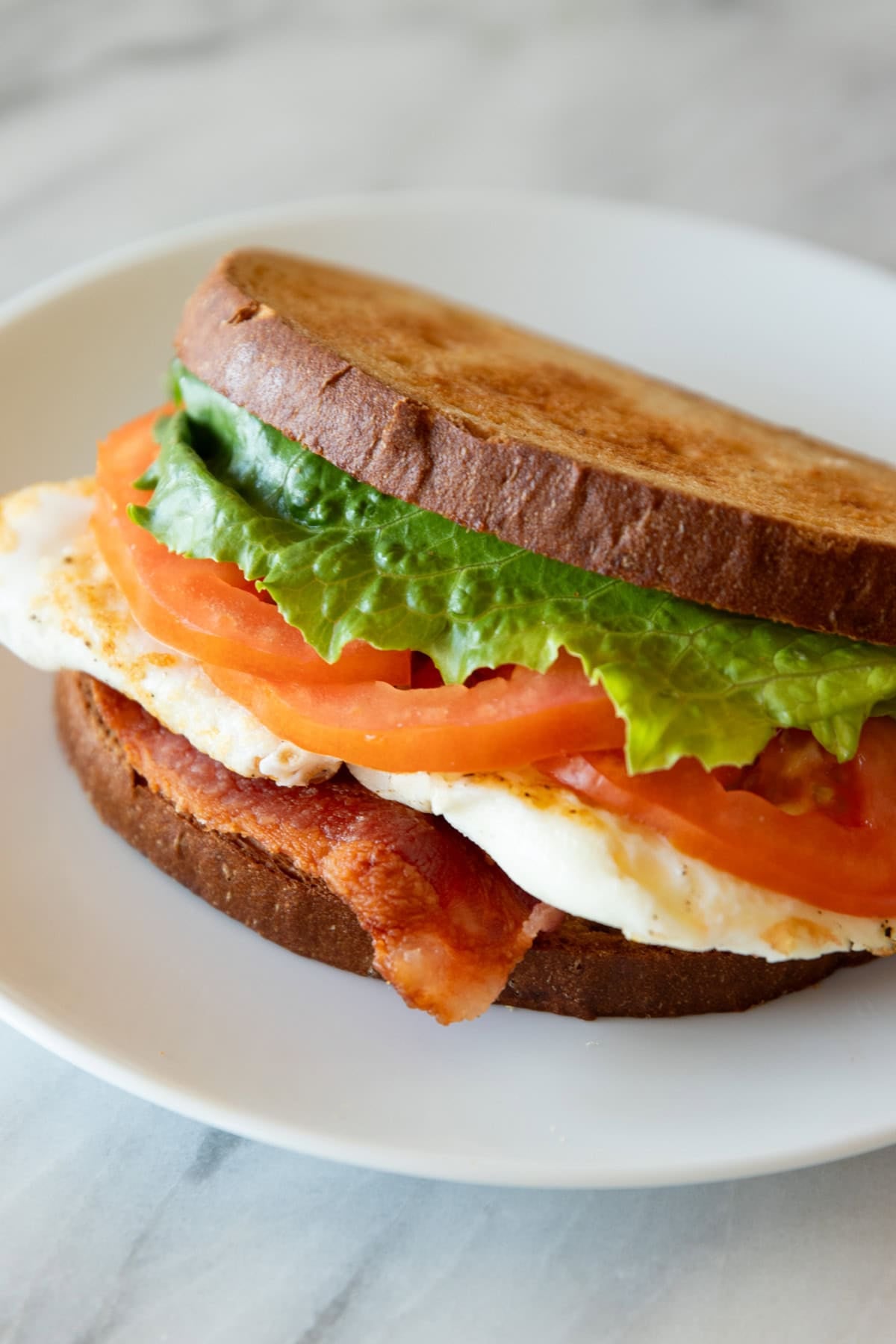 A sandwich made with crispy bacon, romaine lettuce, thinly-sliced tomato, and fried eggs.