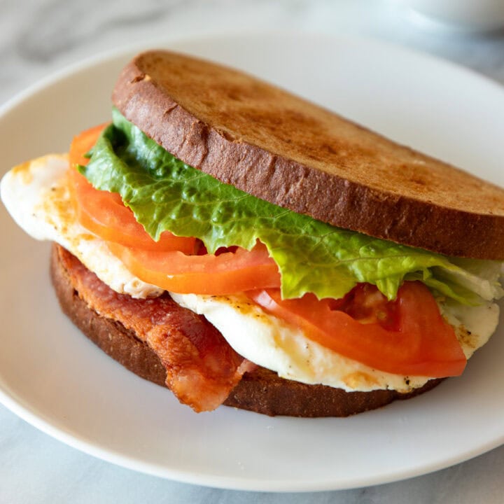A low FODMAP BLT with Egg sandwich sits on a white plate.