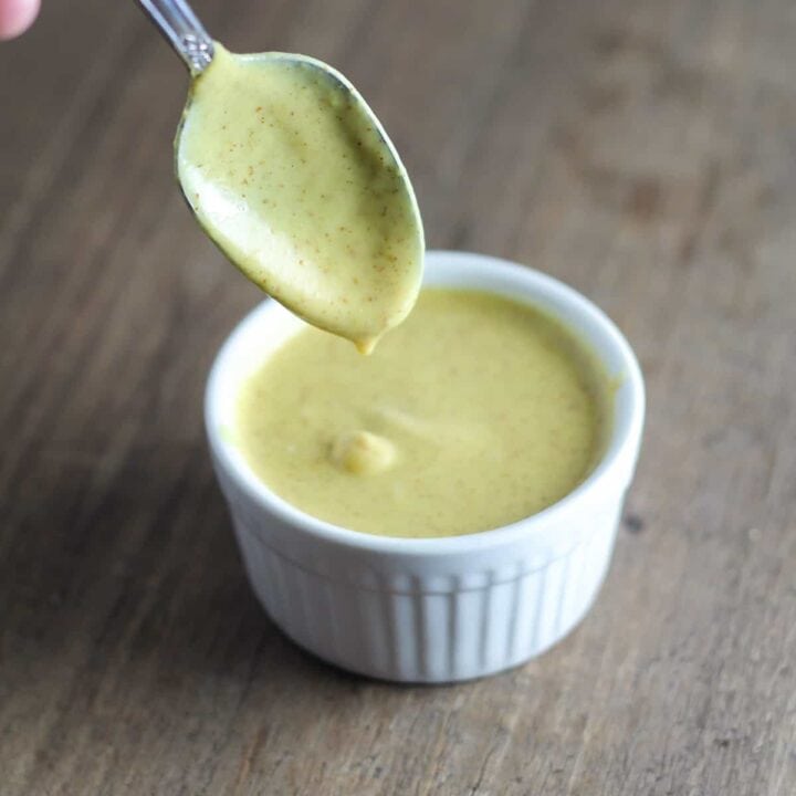 A spoon dipped into a ramekin filled with creamy maple mustard dipping sauce.