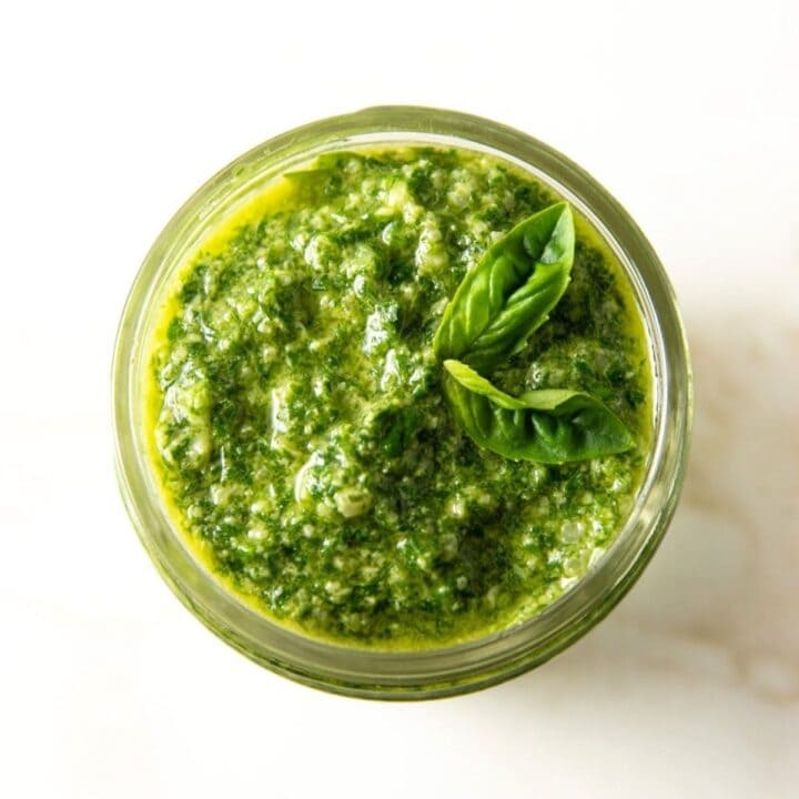 Low FODMAP pesto in a small mason jar topped with fresh basil leaves