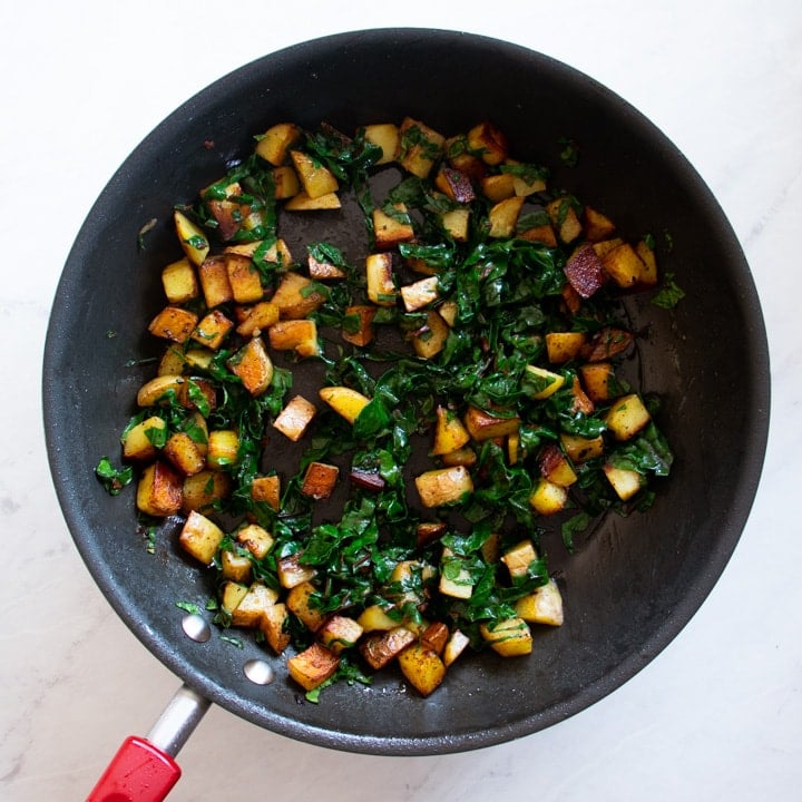 Skillet containing breakfast potatoes, chard, and bacon. 
