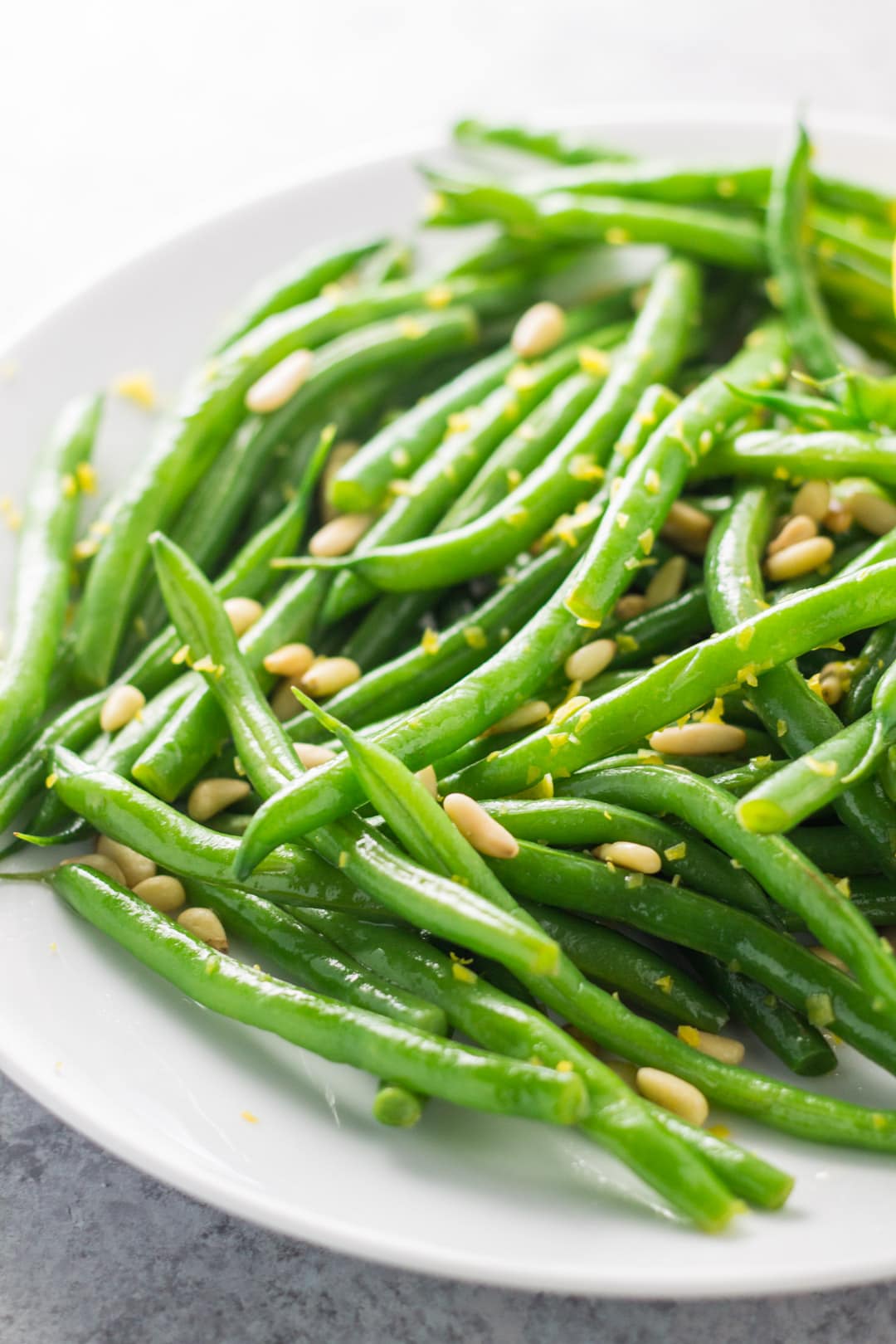 A close-up of green beans with a sprinkle of lemon zest and toasted pine nuts.