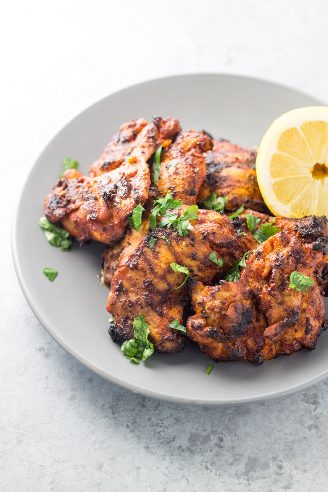 A plate of peri peri grilled chicken thighs with a lemon half.