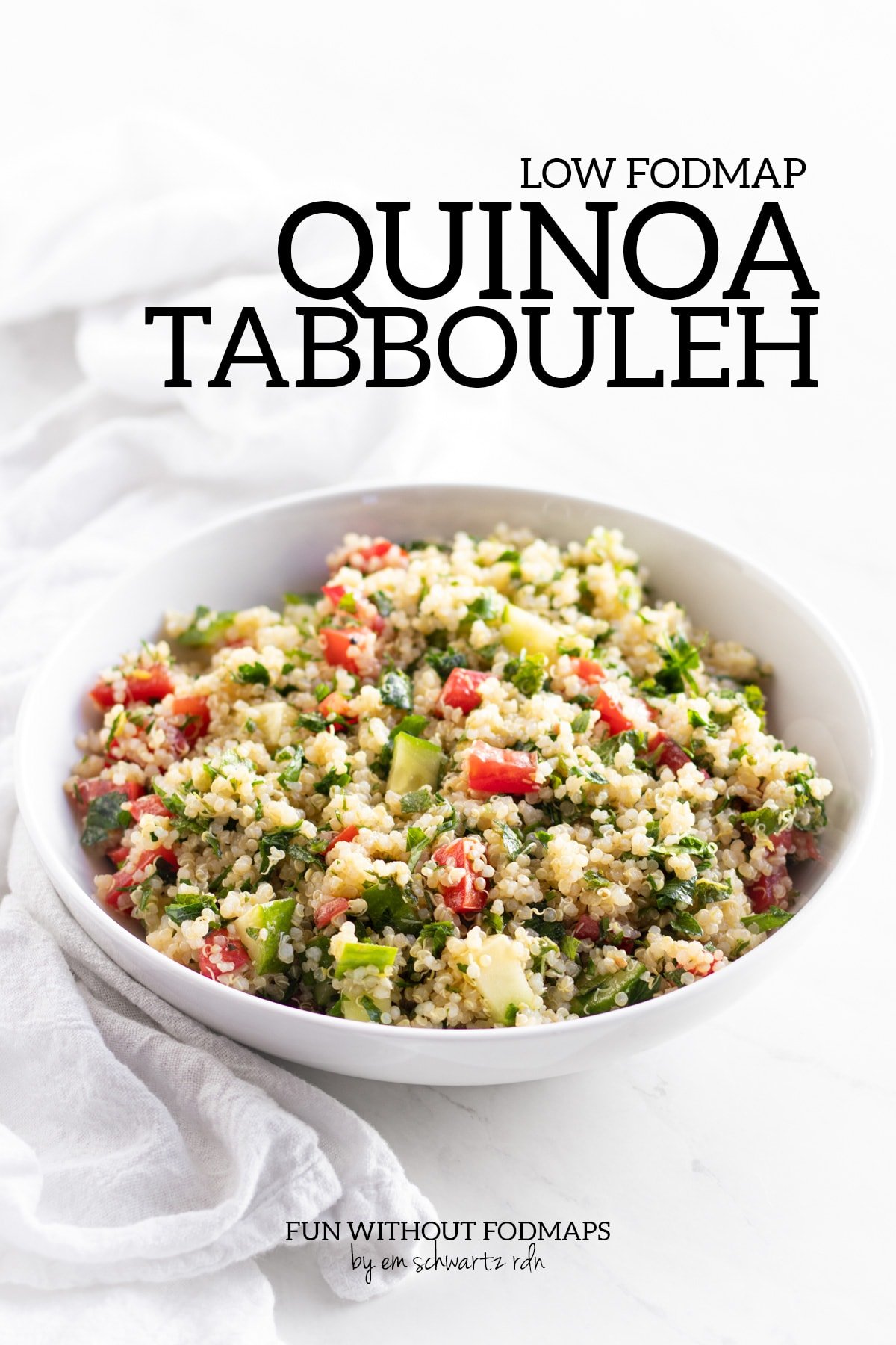 A shallow white bowl filled with a mixture of quinoa, tomato, cucumber, and fresh herbs. The bowl sits on a white marble background with a white cloth napkin on the side. A black text overlay reads Low FODMAP Quinoa Tabbouleh