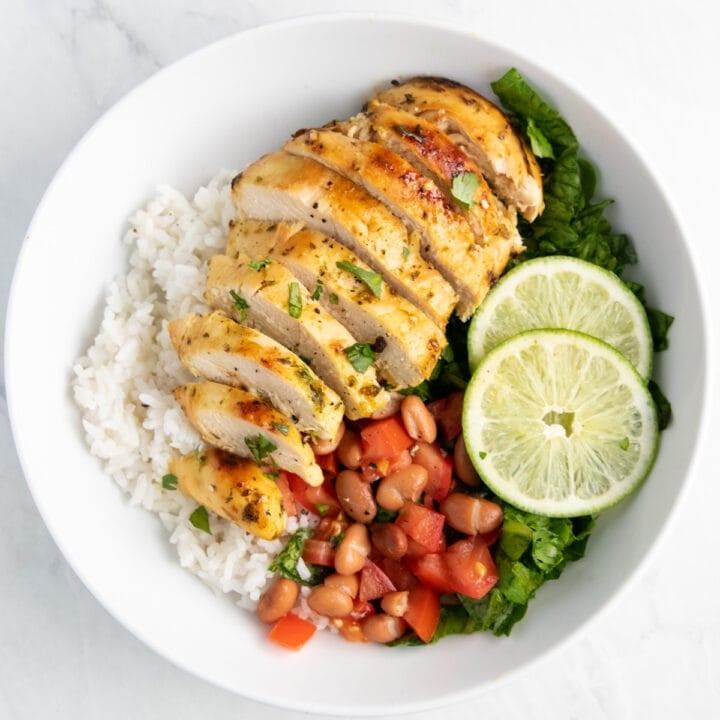 Sliced low FODMAP cilantro lime chicken on top of cooked rice, with lettuce, lime slices, tomatoes, and a small serving of canned pinto beans.