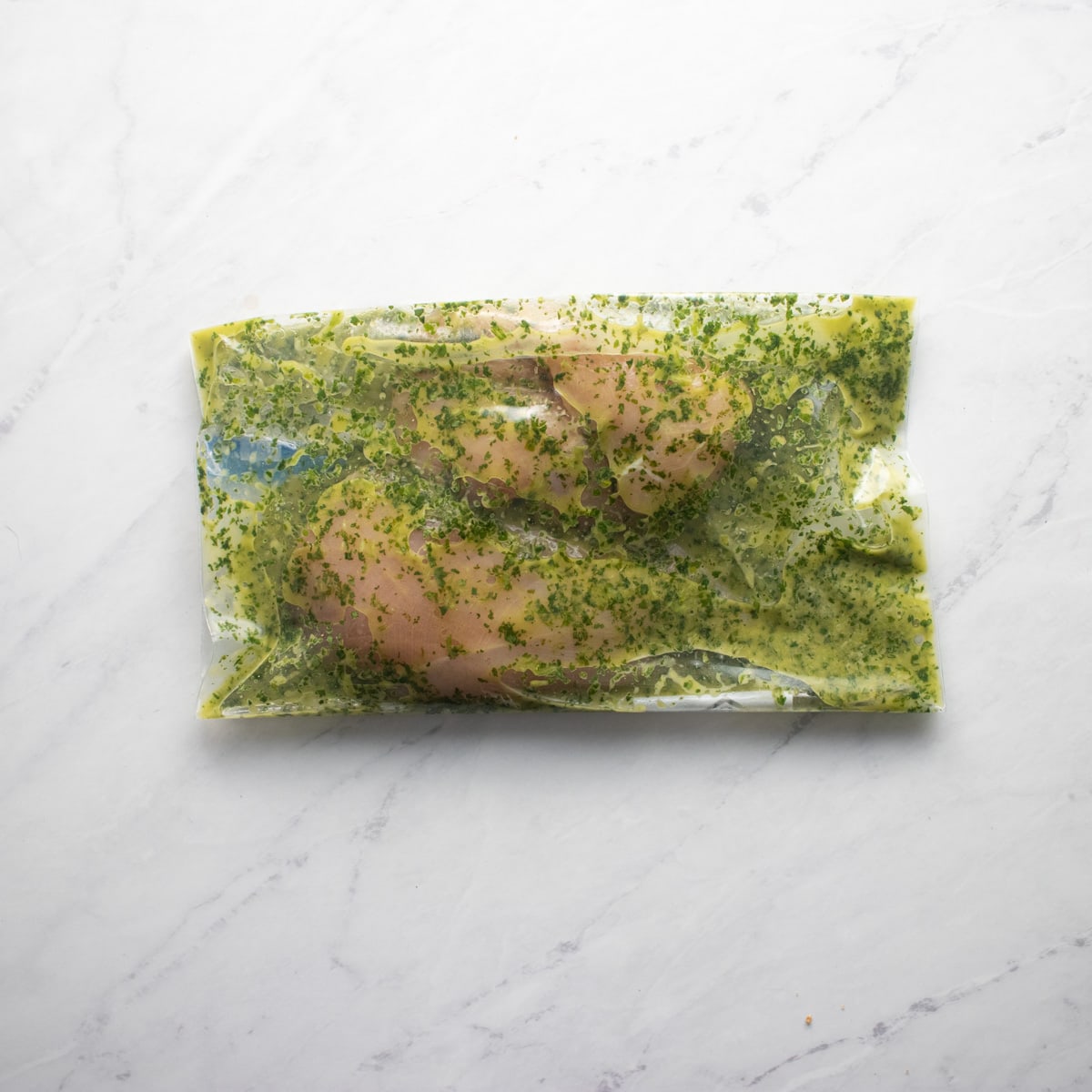 chicken covered in cilantro lime marinade in a sealed ziplock freezer bag