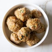 A shallow white bowl filled with low FODMAP pesto turkey meatballs sitting on a white counter.