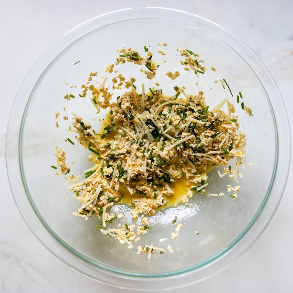 Quick oats mixed with egg, low FODMAP milk, herbs, and Parmesan in a large glass bowl.