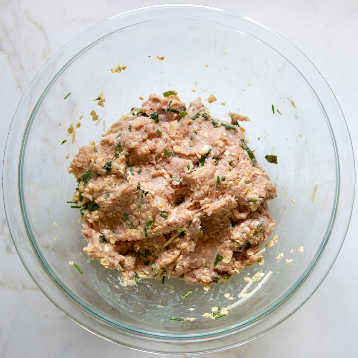Ground turkey is mixed with the soaked oats, herbs, and cheese ready to form meatballs.