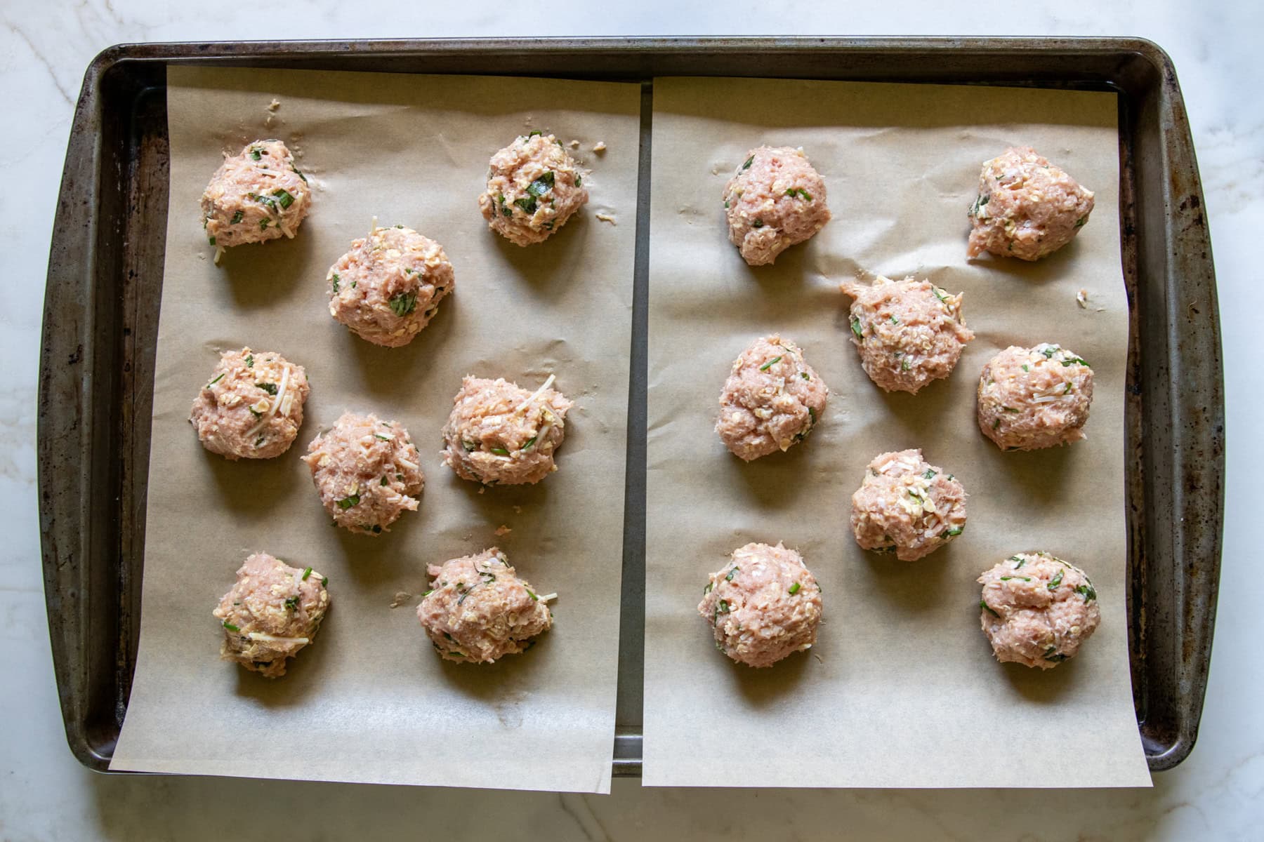 Meatballs are formed and placed on a parchment lined baking sheet ready for the oven.