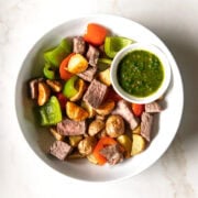 Looking down into a plate filled with Low FODMAP Steak and Potatoes with a small condiment dish filled with an IBS-friendly chimichurri.