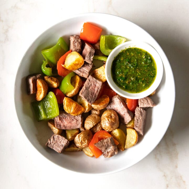 Looking down into a plate filled with Low FODMAP Steak and Potatoes with a small condiment dish filled with an IBS-friendly chimichurri.