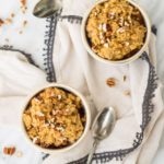 Bowls of Low FODMAP Pumpkin Pie Oatmeal surrounded by antique spoons and chopped pecans.