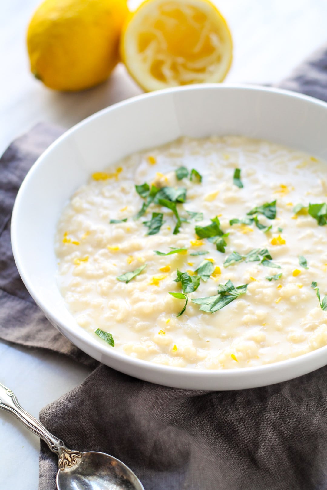 A white bowl filled with a lemony rice and chicken soup and topped with fresh parsley and lemon zest.