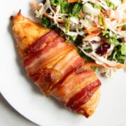 A close up of a bacon wrapped chicken breast next to a serving of low FODMAP sunflower crunch salad.