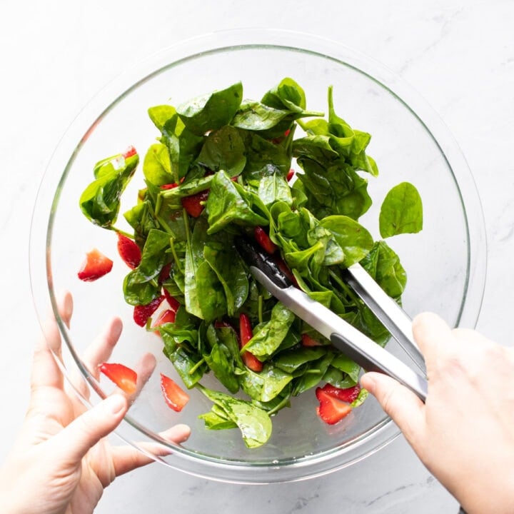 Tossing spinach and strawberries with balsamic vinaigrette in a large glass mixing bowl