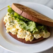 Egg salad sandwiched between two slices of toasted gluten-free bread and a lettuce leaf.