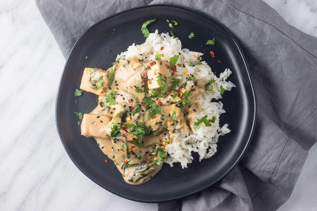 A black plate filled with tofu tossed in a creamy peanut-coconut milk sauce over rice.