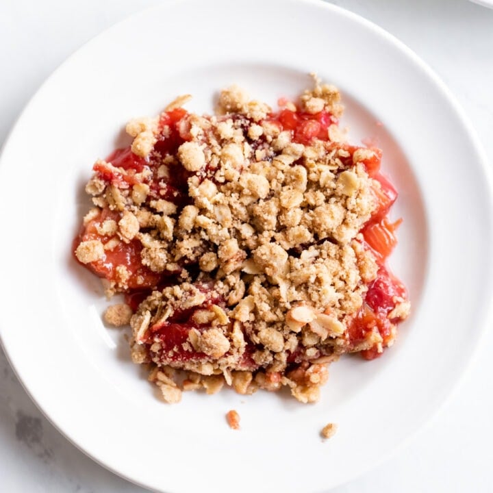 A serving of low FODMAP strawberry rhubarb crumble is served on a small white plate.