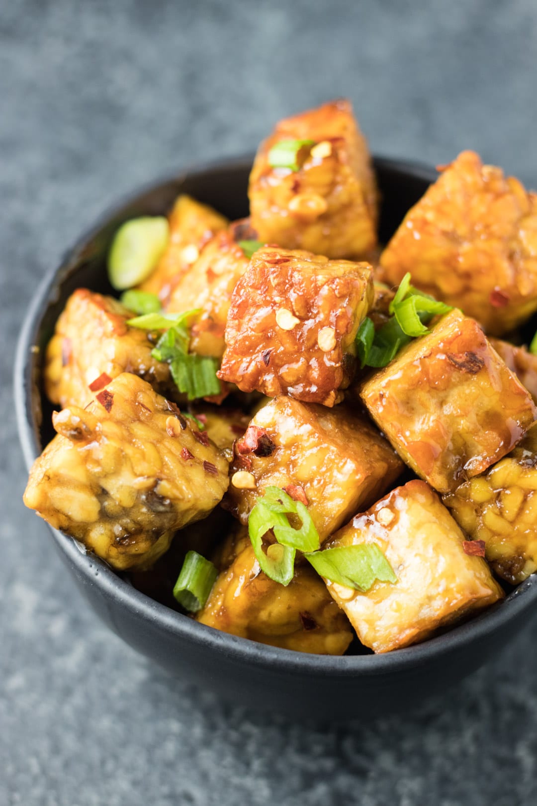 A bowl of seared tempeh cubes tossed in a maple-soy glaze and topped with sliced green onions