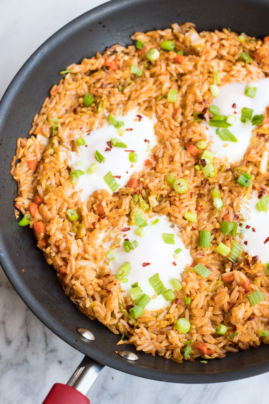 A close up of Indonesian fried rice and eggs topped with sliced green onion tops and red chili flakes.