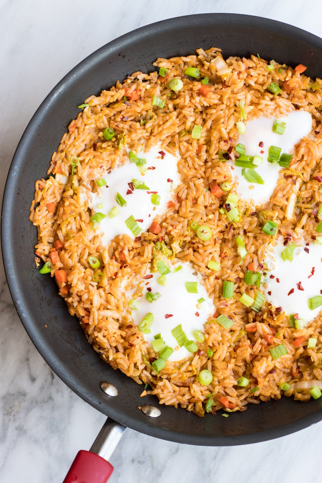 A skillet filled with fried rice and fried eggs topped with sliced green onion tops and red chili flakes.