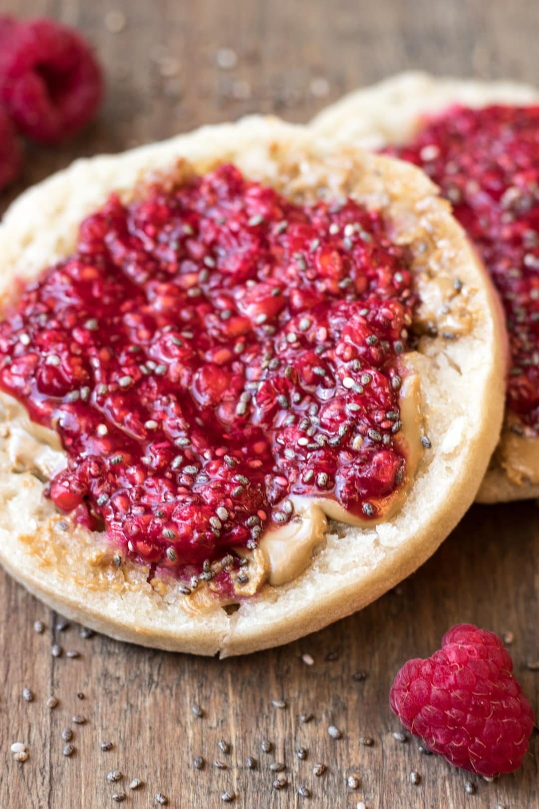 Two toasted brown rice English muffin halves topped with peanut butter and raspberry chia jam.