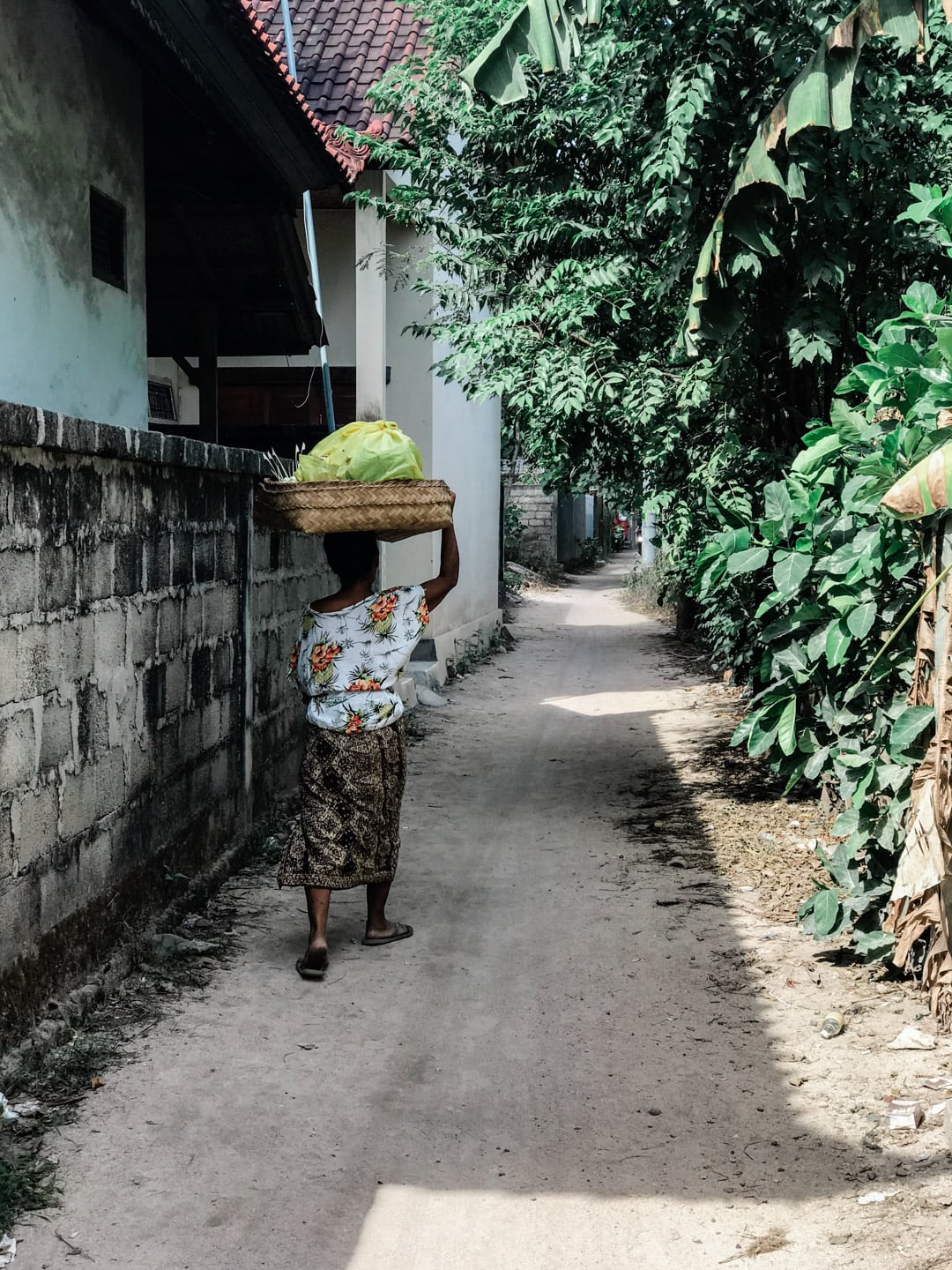 A local Lembongan woman carries a basket her head as she walks down an alley.