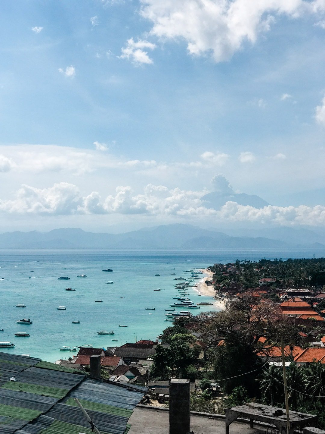 A view overlooking the beach in Lembongan, Bali, Indonesia. A volcano peeks through the clouds in the distance.