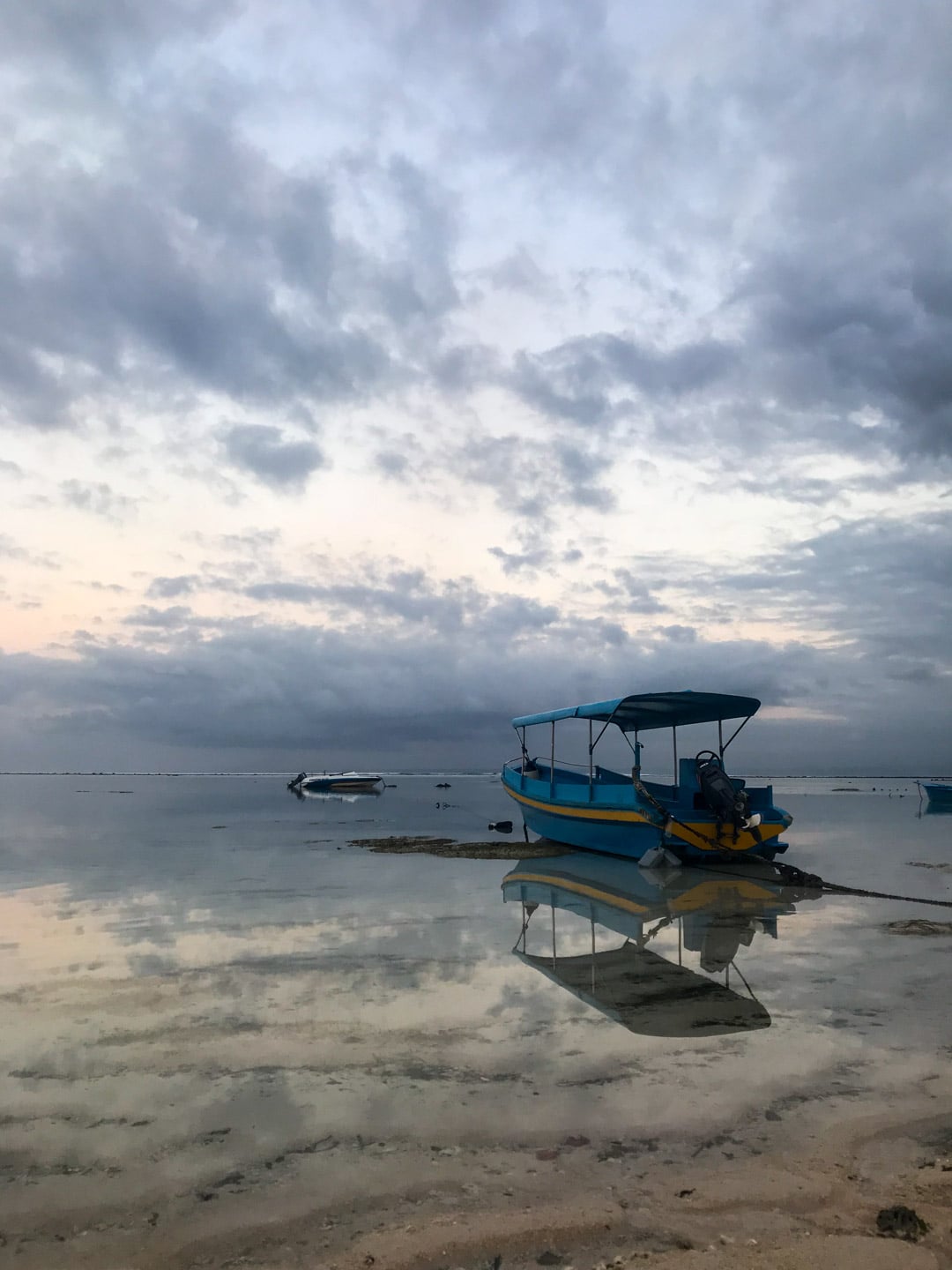 Still water reflects the sky and boat in Lembongan