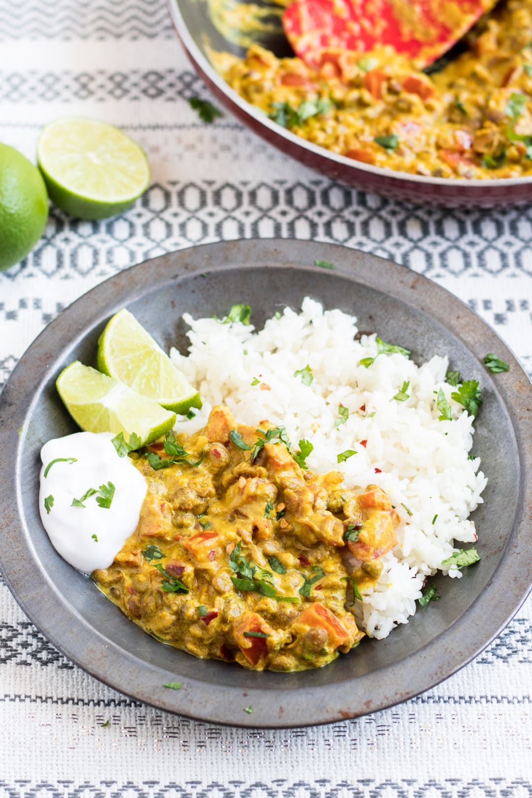 A metal bowl filled with low FODMAP lentil dal and basmati rice garnished with cilantro and served with lime wedges and a dollop of coconut yogurt.