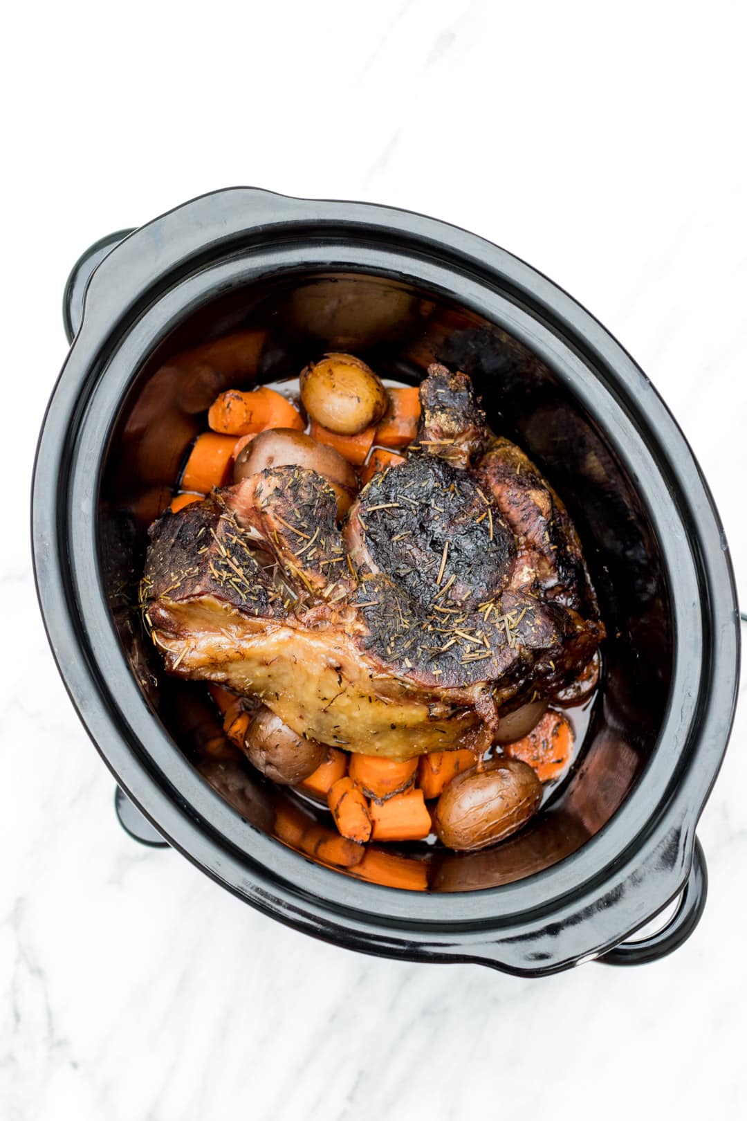 A crockpot filled with potatoes, carrots, and beef roast.