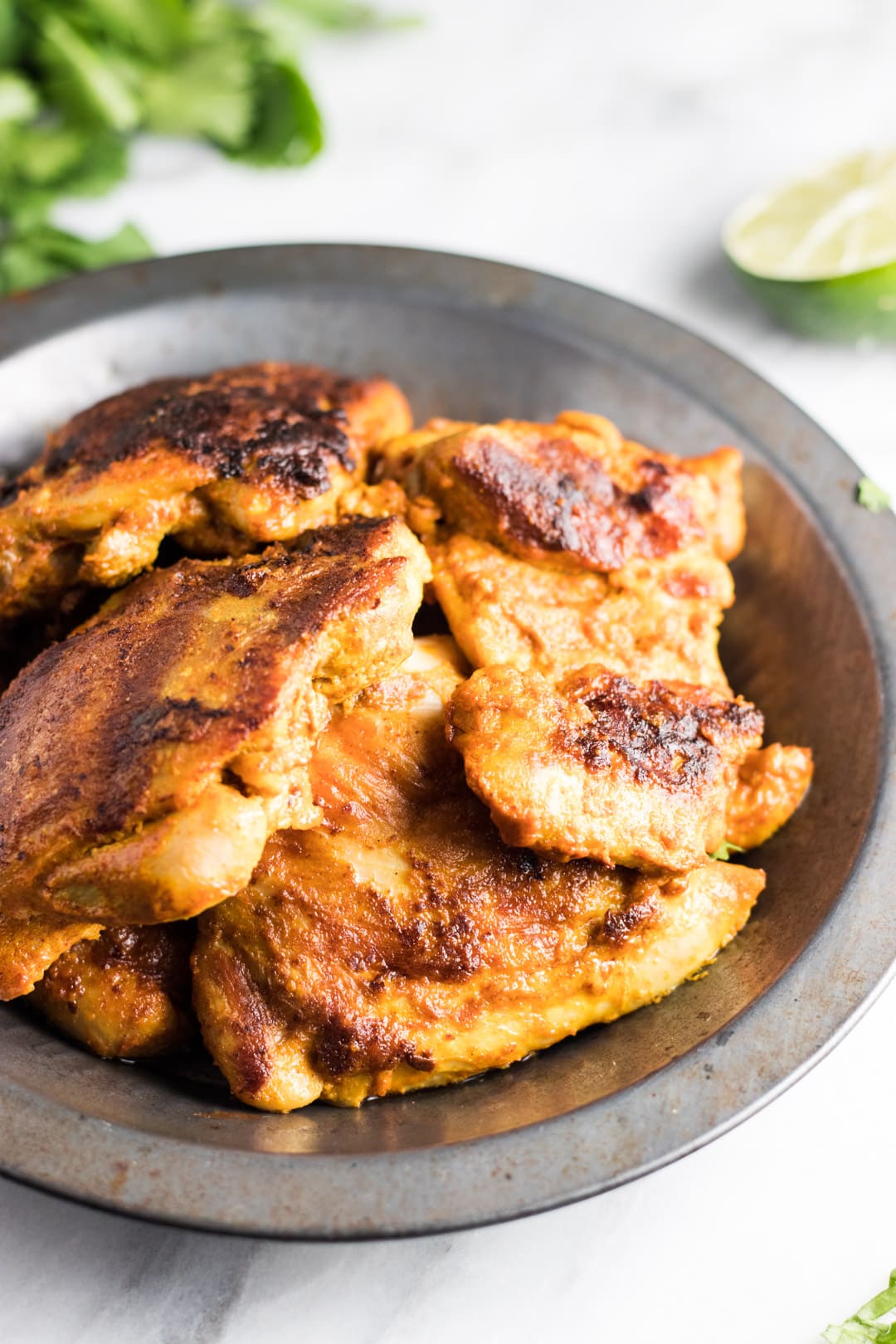 A close up of grilled tandoori-inspired chicken in a metal bowl. 